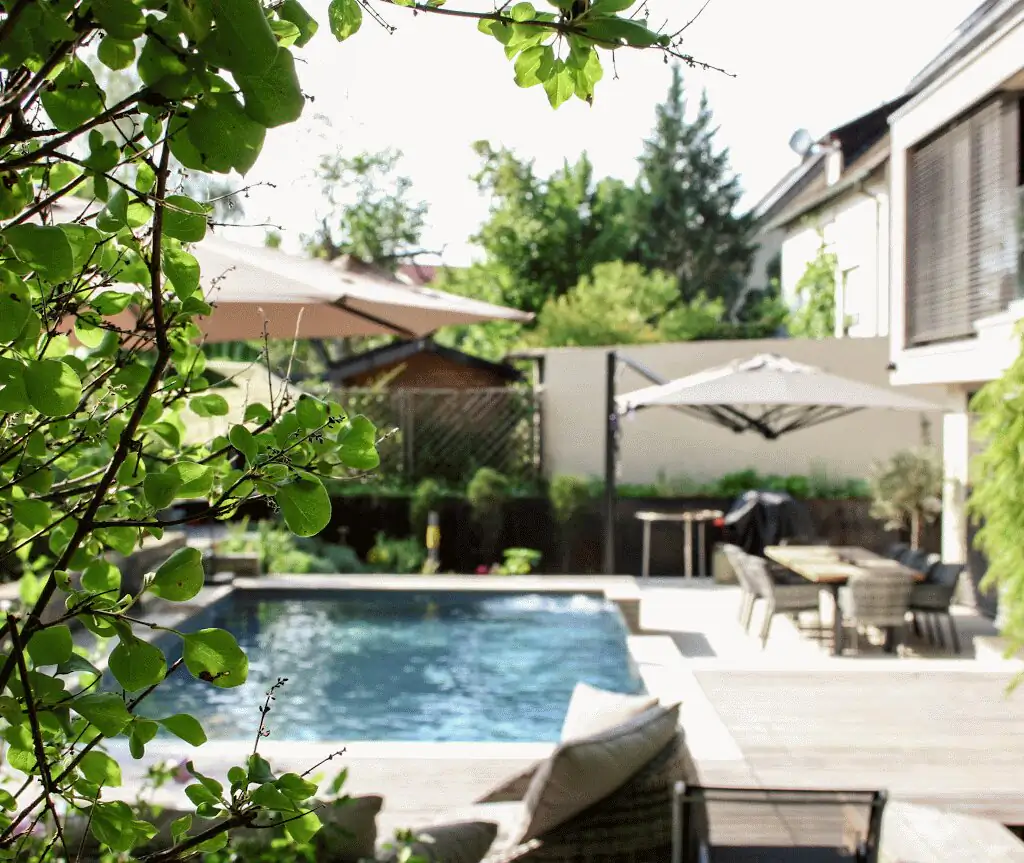 Garden view through foliage to the pool and dining area in Villingen-Schwenningen