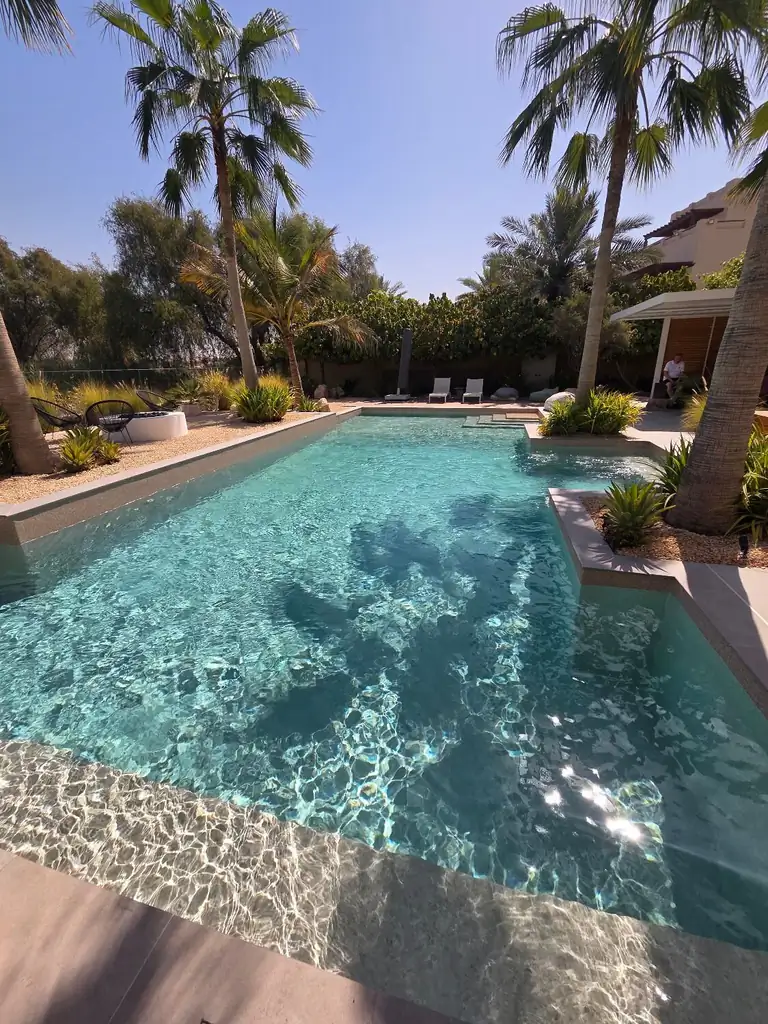 Resort pool under palms with sun ledge and shallow entry in sunlight in Dubai